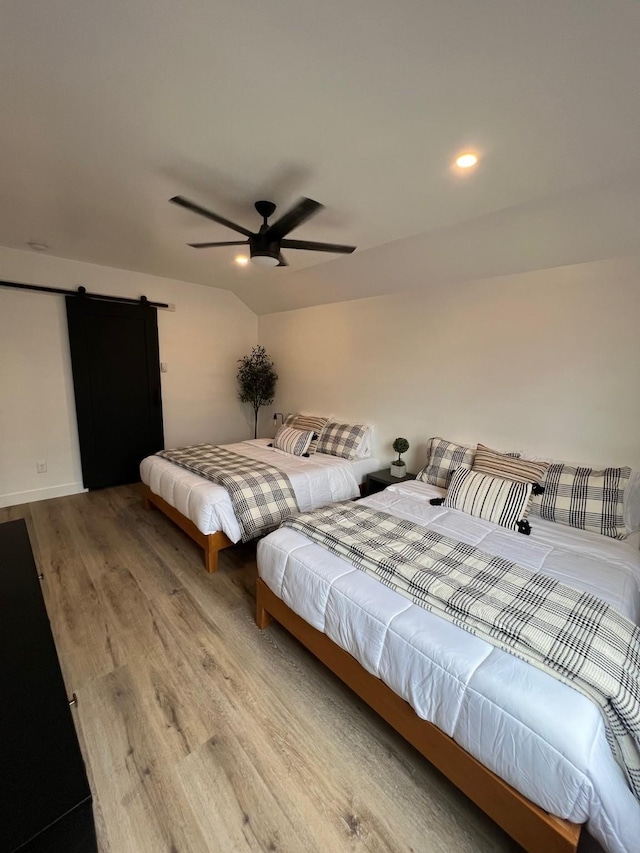 bedroom featuring ceiling fan, light wood-type flooring, vaulted ceiling, and a barn door