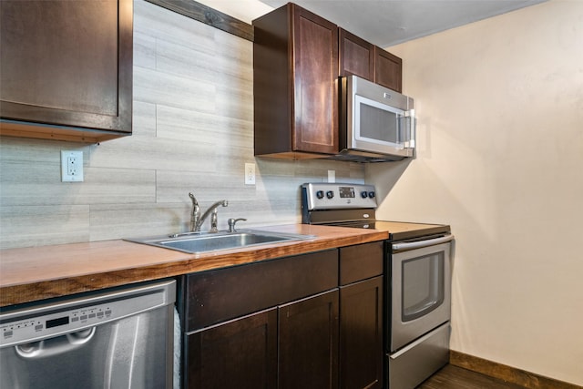 kitchen featuring stainless steel appliances, tasteful backsplash, wood counters, dark brown cabinets, and sink