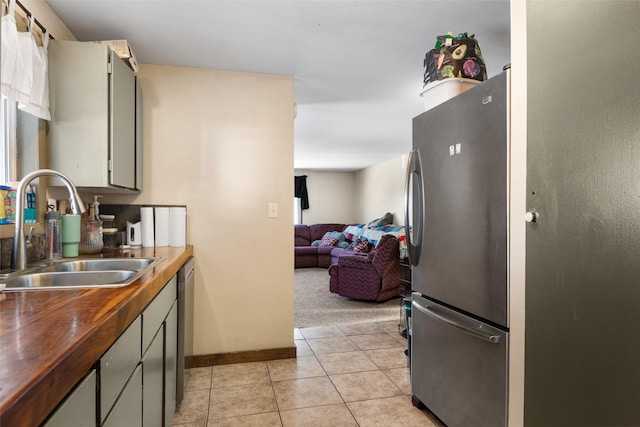 kitchen featuring stainless steel appliances, butcher block countertops, gray cabinetry, light carpet, and sink