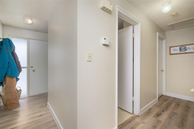 hallway with a textured ceiling and light hardwood / wood-style flooring