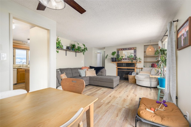 living room featuring light wood-type flooring, ceiling fan, a fireplace, a textured ceiling, and sink