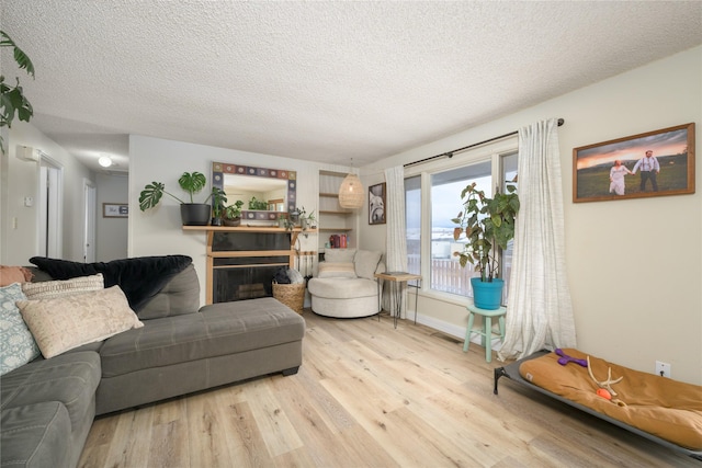 living room with a textured ceiling, a fireplace, and light hardwood / wood-style flooring