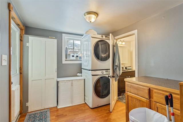 clothes washing area with light hardwood / wood-style flooring and stacked washer / drying machine