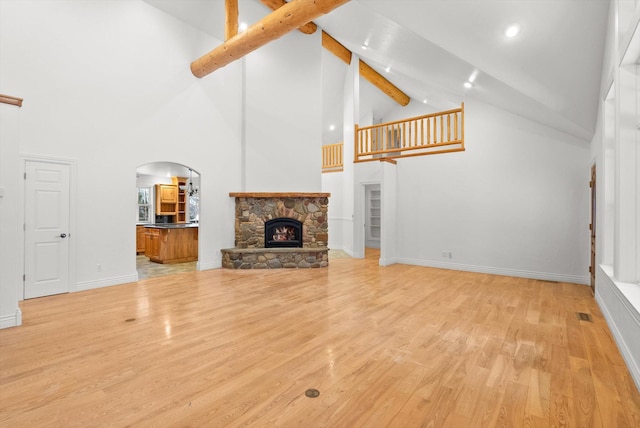 unfurnished living room featuring beam ceiling, light hardwood / wood-style flooring, a stone fireplace, and high vaulted ceiling