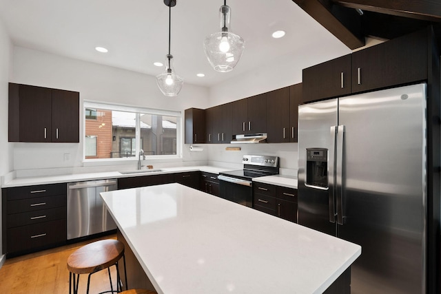 kitchen featuring appliances with stainless steel finishes, a center island, a kitchen bar, sink, and decorative light fixtures