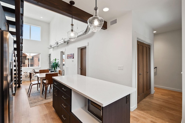 kitchen with hanging light fixtures, stainless steel fridge with ice dispenser, a center island, dark brown cabinetry, and light hardwood / wood-style flooring