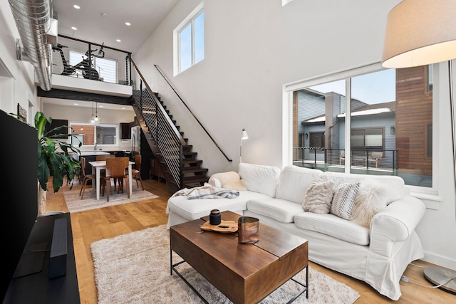 living room with a high ceiling, a healthy amount of sunlight, and light hardwood / wood-style flooring