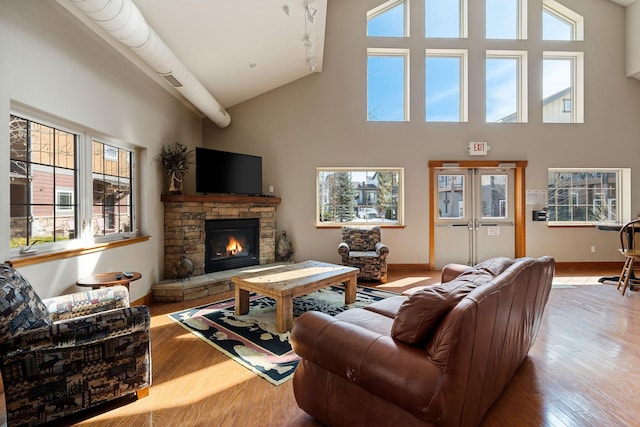 living room with light wood-type flooring, a stone fireplace, and a towering ceiling