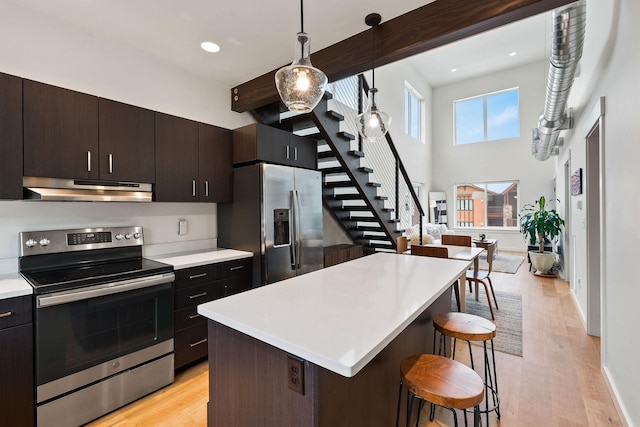 kitchen featuring a kitchen breakfast bar, appliances with stainless steel finishes, hanging light fixtures, light hardwood / wood-style floors, and a kitchen island