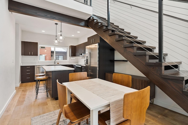 dining area featuring sink, light wood-type flooring, and beam ceiling