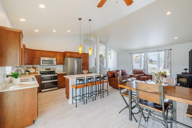 kitchen with a kitchen bar, a sink, appliances with stainless steel finishes, light countertops, and a wood stove