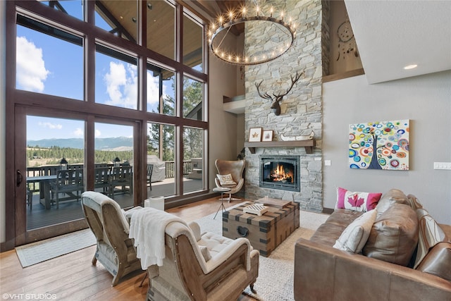 living room with an inviting chandelier, a fireplace, a towering ceiling, light wood-type flooring, and a mountain view