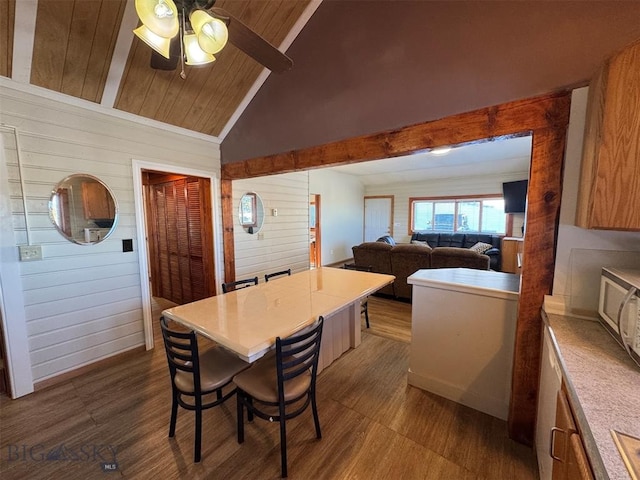 dining room with vaulted ceiling, ceiling fan, wooden walls, and dark hardwood / wood-style flooring