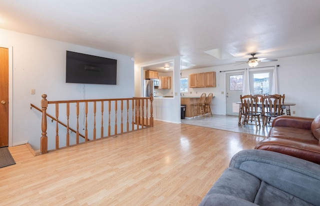 living room with light wood-type flooring, ceiling fan, and a skylight