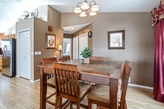 dining space with lofted ceiling, a notable chandelier, and light hardwood / wood-style floors