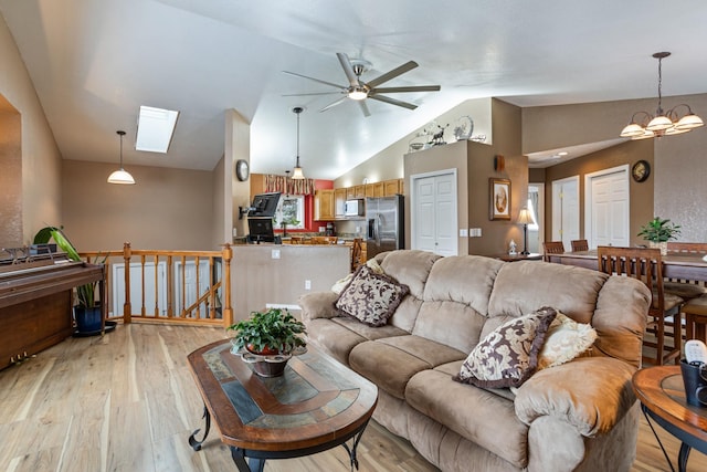 living room with light hardwood / wood-style floors, ceiling fan with notable chandelier, and vaulted ceiling with skylight