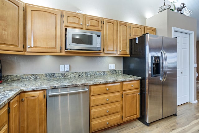 kitchen with stainless steel appliances, light wood-type flooring, and light stone counters