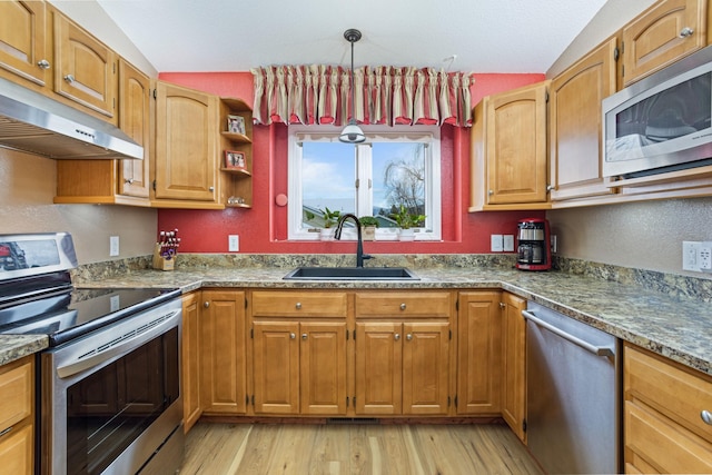 kitchen featuring sink, light wood-type flooring, dark stone counters, pendant lighting, and appliances with stainless steel finishes