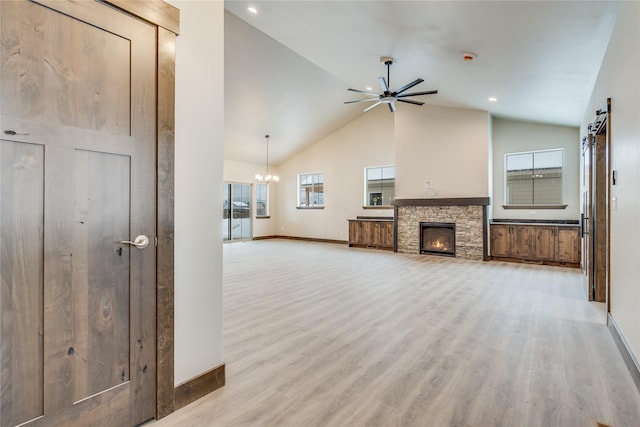 unfurnished living room with light hardwood / wood-style flooring, a stone fireplace, a barn door, and plenty of natural light