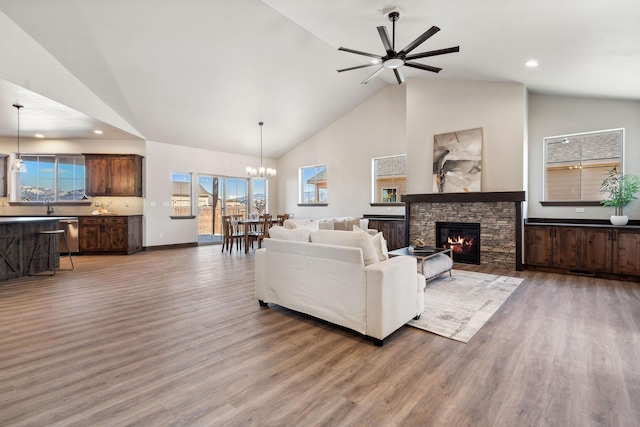 living room with high vaulted ceiling, recessed lighting, an inviting chandelier, a stone fireplace, and light wood finished floors