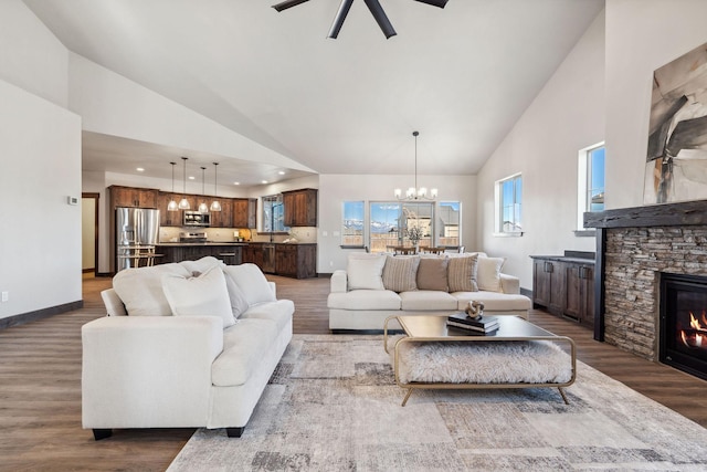 living area with dark wood-style floors, a stone fireplace, high vaulted ceiling, and baseboards