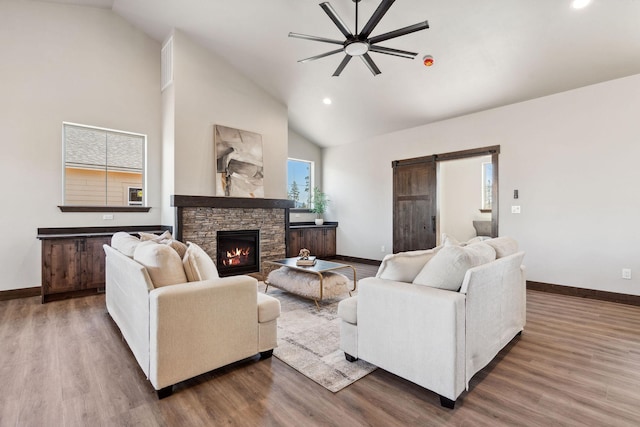 living room featuring a fireplace, a barn door, wood finished floors, and baseboards