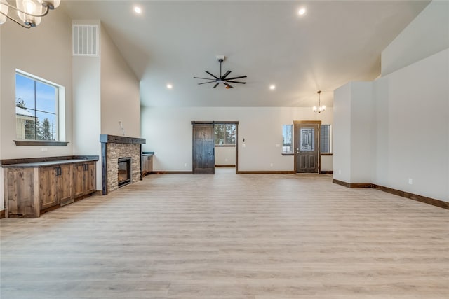 unfurnished living room featuring ceiling fan with notable chandelier, a fireplace, a healthy amount of sunlight, and light hardwood / wood-style flooring