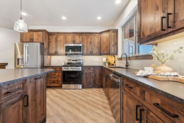 kitchen with light wood-style flooring, a sink, appliances with stainless steel finishes, decorative light fixtures, and tasteful backsplash