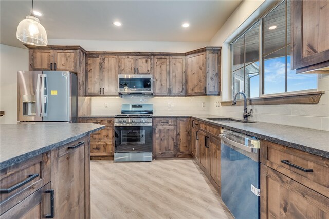 kitchen with sink, light hardwood / wood-style floors, backsplash, pendant lighting, and appliances with stainless steel finishes