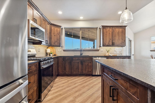 kitchen featuring light wood-style flooring, appliances with stainless steel finishes, dark countertops, decorative light fixtures, and tasteful backsplash