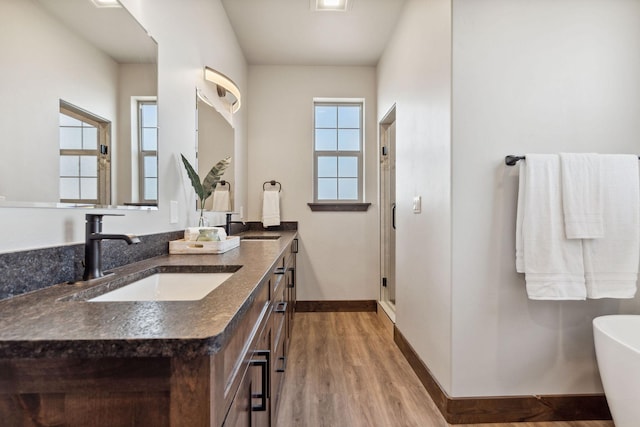 full bathroom with a freestanding tub, a stall shower, wood finished floors, baseboards, and vanity