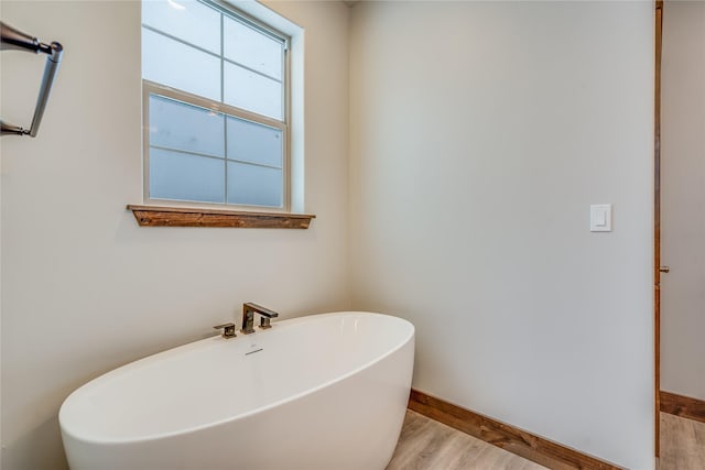 full bath with a freestanding tub, wood finished floors, and baseboards