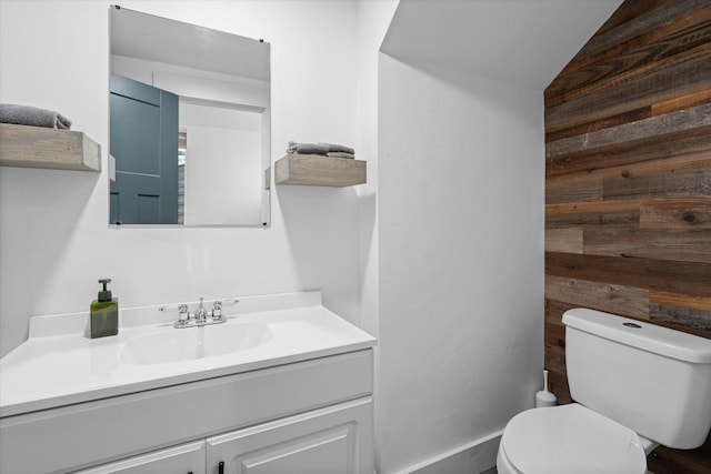 bathroom with wooden walls, toilet, vanity, and lofted ceiling