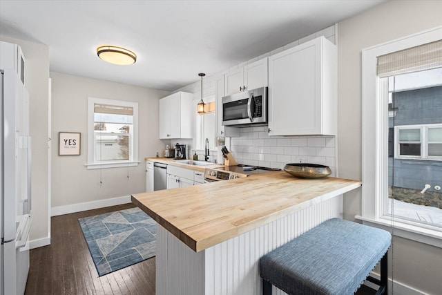 kitchen with tasteful backsplash, butcher block countertops, stainless steel appliances, white cabinetry, and a sink