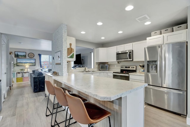 kitchen with sink, white cabinets, kitchen peninsula, a breakfast bar area, and appliances with stainless steel finishes