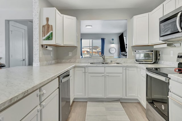 kitchen featuring appliances with stainless steel finishes, light wood-type flooring, light stone counters, white cabinets, and sink