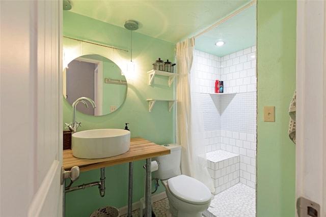 bathroom with sink, a tile shower, and toilet