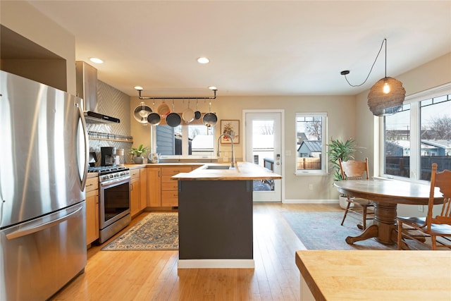 kitchen featuring stainless steel appliances, light wood-type flooring, pendant lighting, sink, and wall chimney range hood