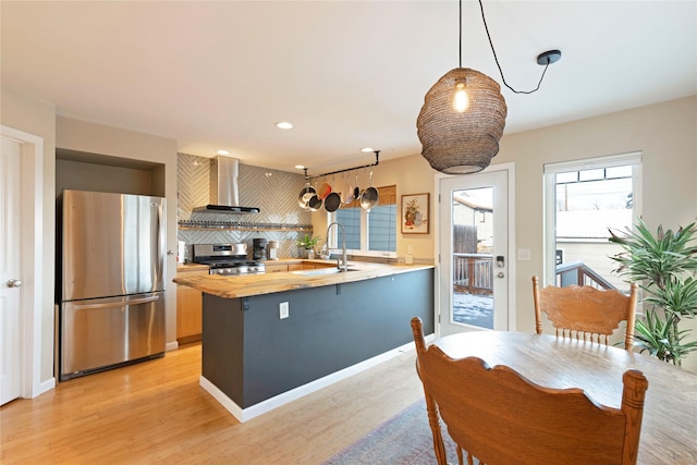 kitchen featuring wall chimney exhaust hood, hanging light fixtures, stainless steel appliances, decorative backsplash, and sink