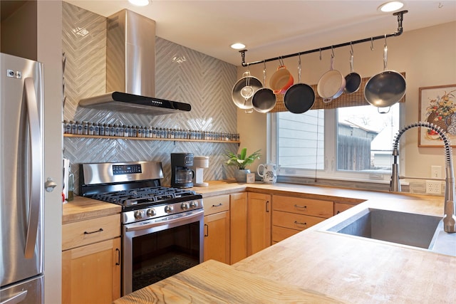 kitchen featuring appliances with stainless steel finishes, wall chimney range hood, butcher block countertops, and sink