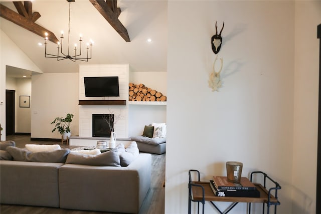 living room with lofted ceiling with beams, wood-type flooring, a large fireplace, and a chandelier