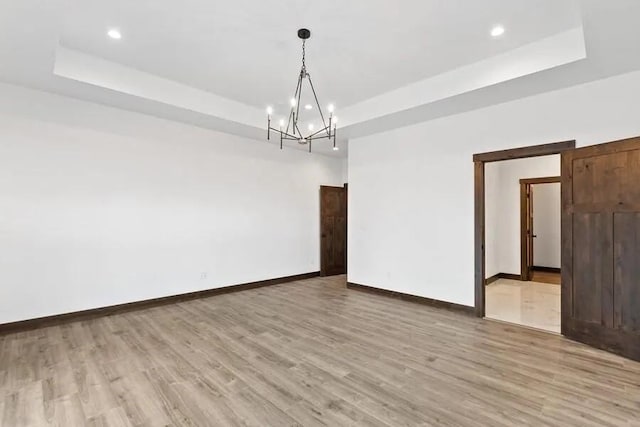 spare room with an inviting chandelier, light wood-type flooring, and a tray ceiling