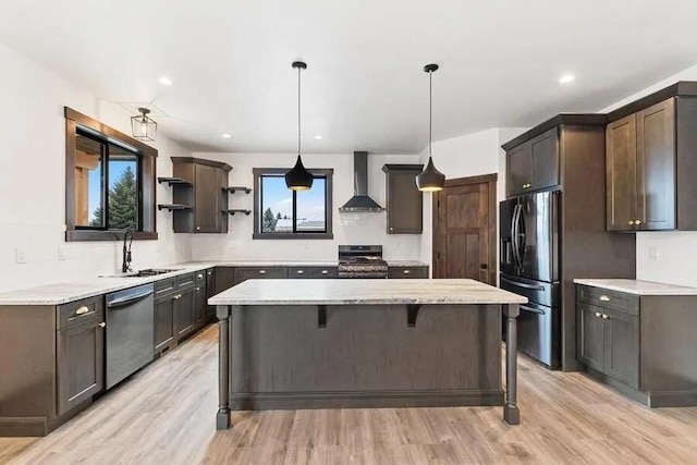 kitchen with wall chimney exhaust hood, sink, hanging light fixtures, appliances with stainless steel finishes, and a kitchen island