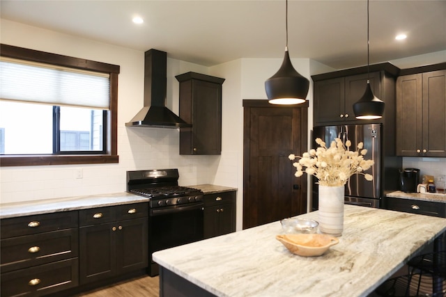 kitchen with stainless steel fridge, black range with gas cooktop, hanging light fixtures, decorative backsplash, and wall chimney exhaust hood