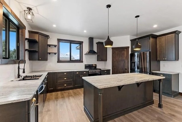 kitchen featuring sink, a kitchen bar, hanging light fixtures, stainless steel appliances, and wall chimney exhaust hood