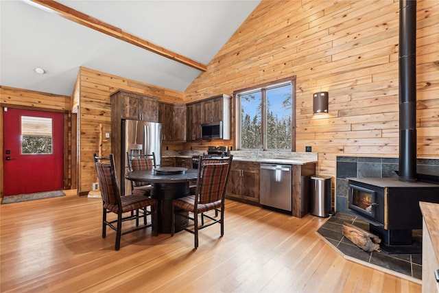 kitchen featuring wood walls, light hardwood / wood-style flooring, dark brown cabinetry, appliances with stainless steel finishes, and a wood stove