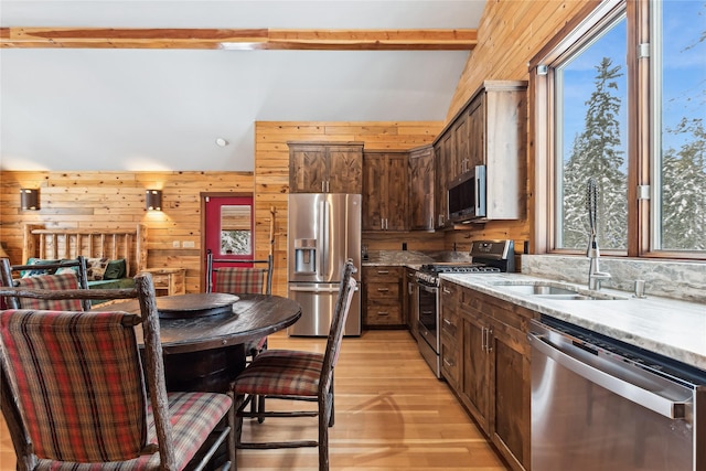 kitchen featuring wood walls, sink, light wood-type flooring, stainless steel appliances, and dark brown cabinets