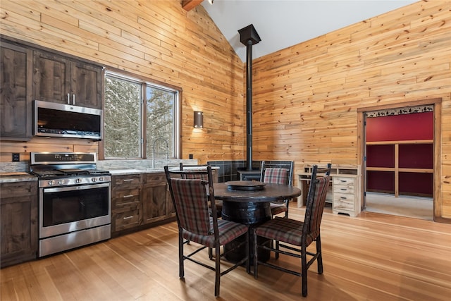 kitchen featuring appliances with stainless steel finishes, wooden walls, light hardwood / wood-style floors, high vaulted ceiling, and dark brown cabinets