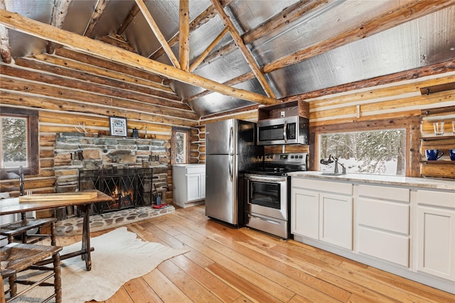 kitchen with rustic walls, white cabinetry, light wood-type flooring, appliances with stainless steel finishes, and a stone fireplace