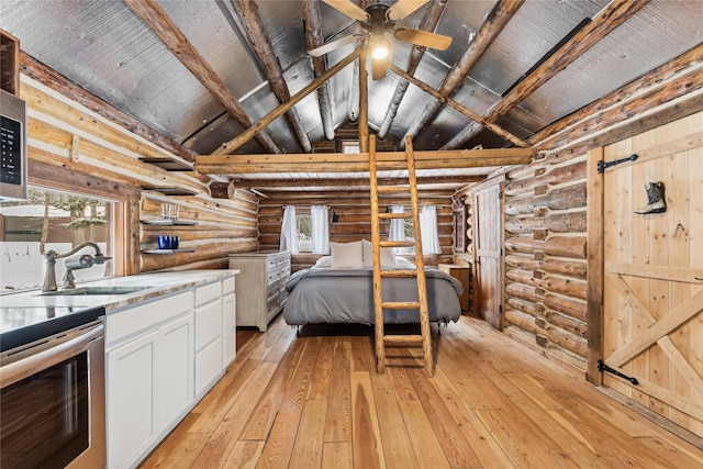 unfurnished bedroom with beamed ceiling, light wood-type flooring, high vaulted ceiling, rustic walls, and sink